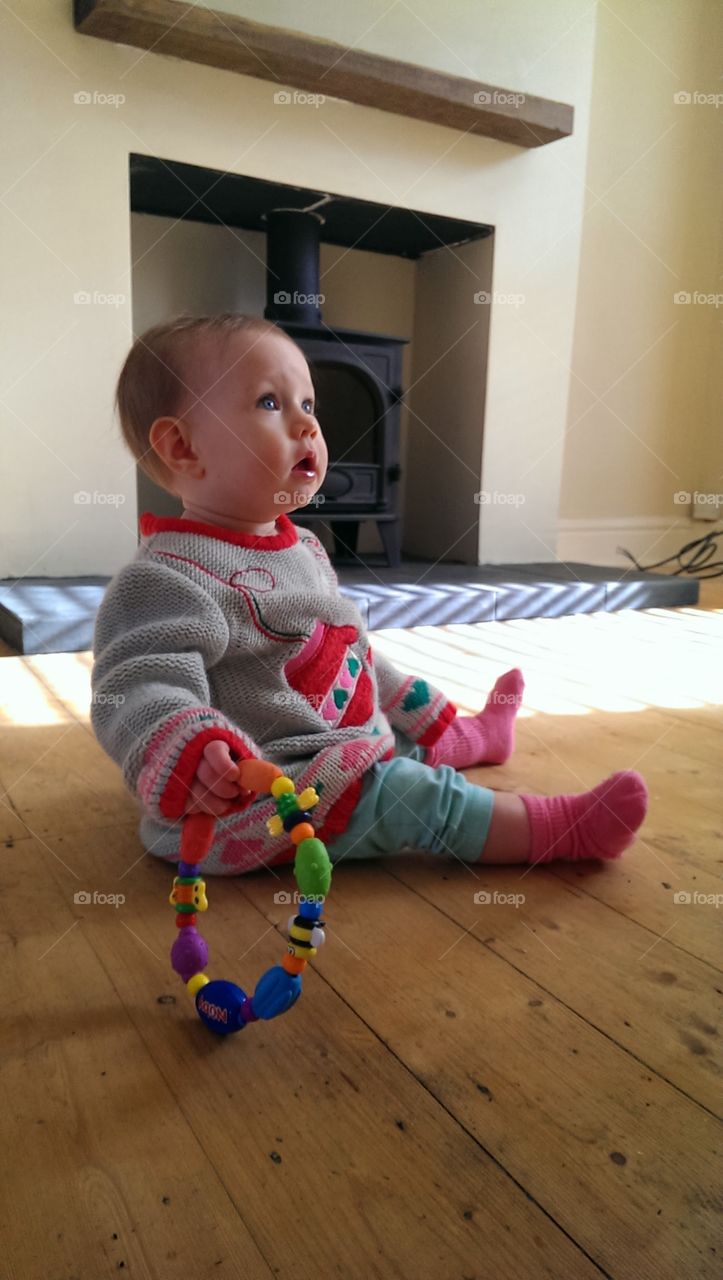 baby sat in empty room with floorboards looking up into sunlight