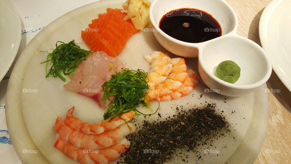 Sasimi raw fish with sliced salmon, shrimps and fresh fish, dipped in soy sauce, wasabi and ginger on a plate.
