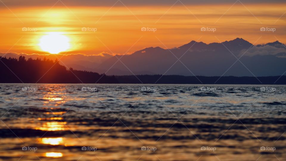 A vibrant sunset over the Olympic Mountain Range illuminates the Puget Sound on a summer day