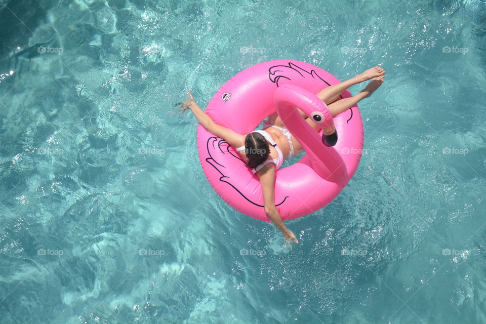 Looking Down on a girl floating on a pink flamingo pool floating a swimming pool.