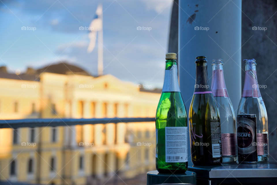 Helsinki, Finland - May 1, 2017: Empty sparkling wine bottles on top of a metallic trash bin outdoors at the Senate Square with the Finnish Government Palace and Finnish flag on the background on the evening May Day celebrations in Helsinki, Finland.