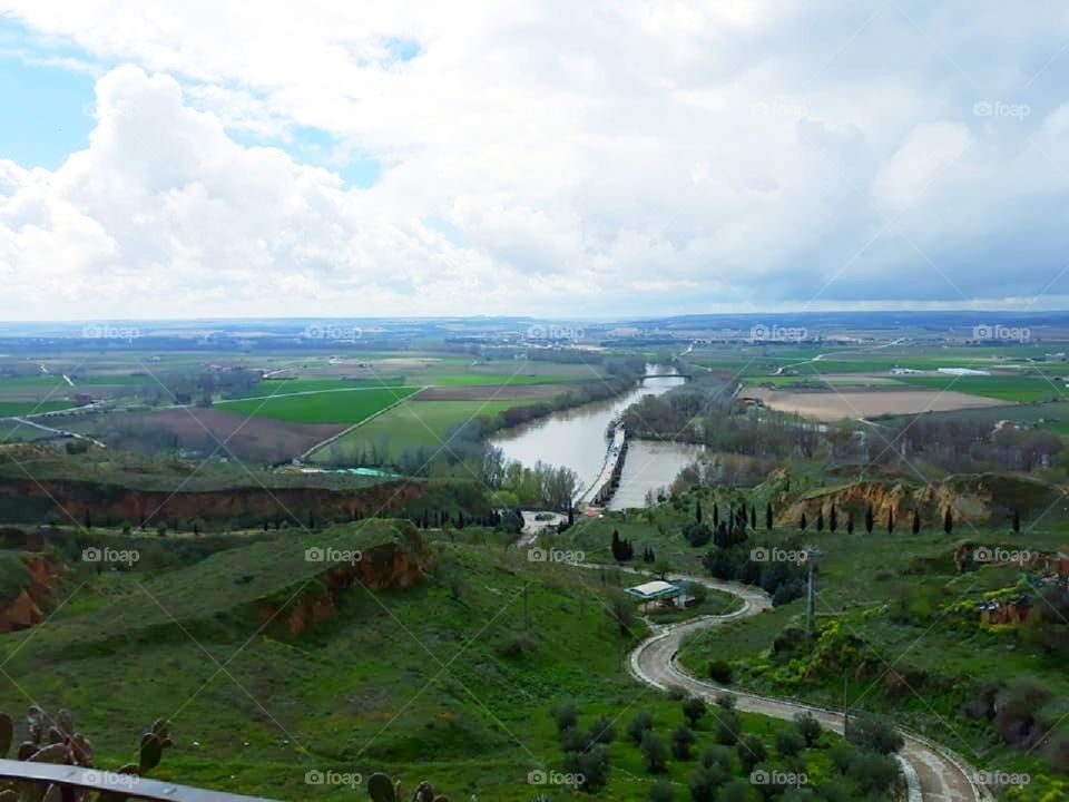 Looking out over a lone river and vacant farmland.  Various textures of greenery dominate the landscape.