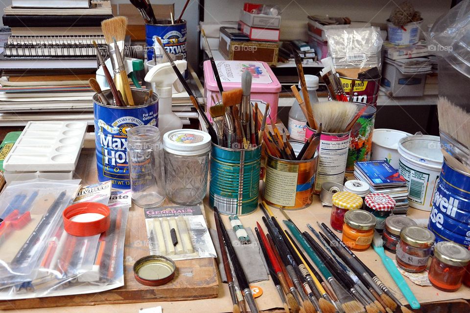 A table is seem with paintbrushes, paint and other artist supplies