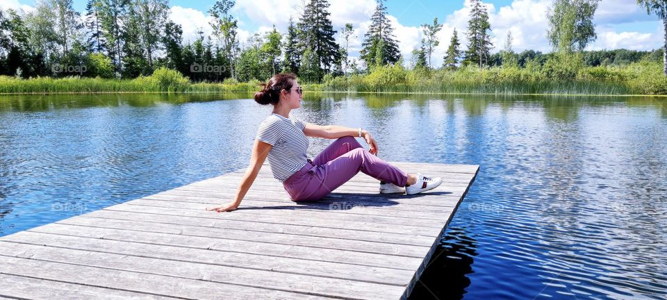 Girl sitting on a pier near a lake in summer