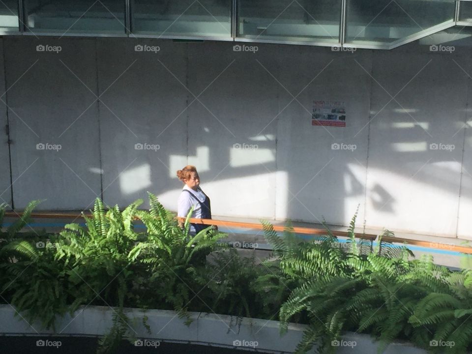 A woman walking in the train station. Sun, shadows and plants
