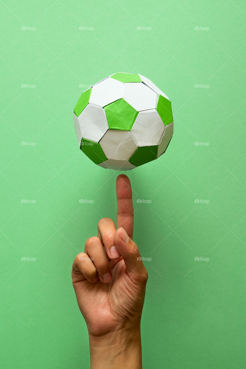 Hand spinning paper soccer ball on green background. Origami. Paper craft. Soccer game concept.