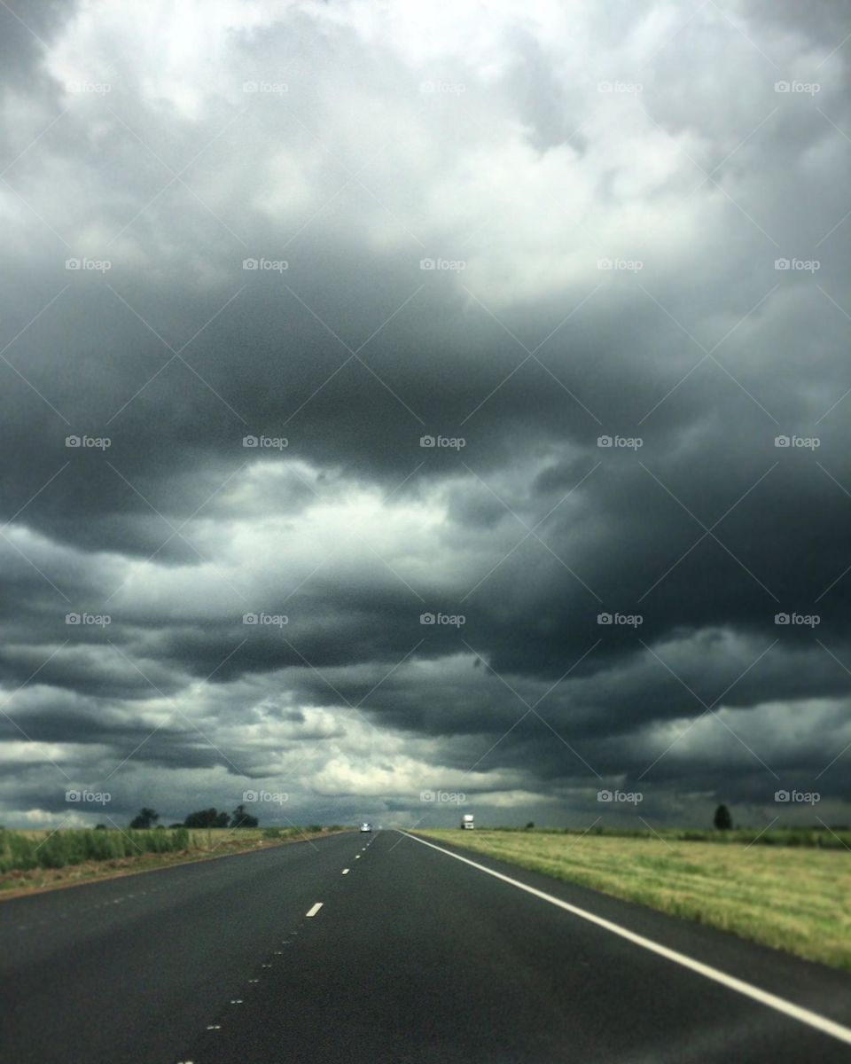 On the highway through the oncoming storm, dark clouds stretching over the grasslands and the road between. 