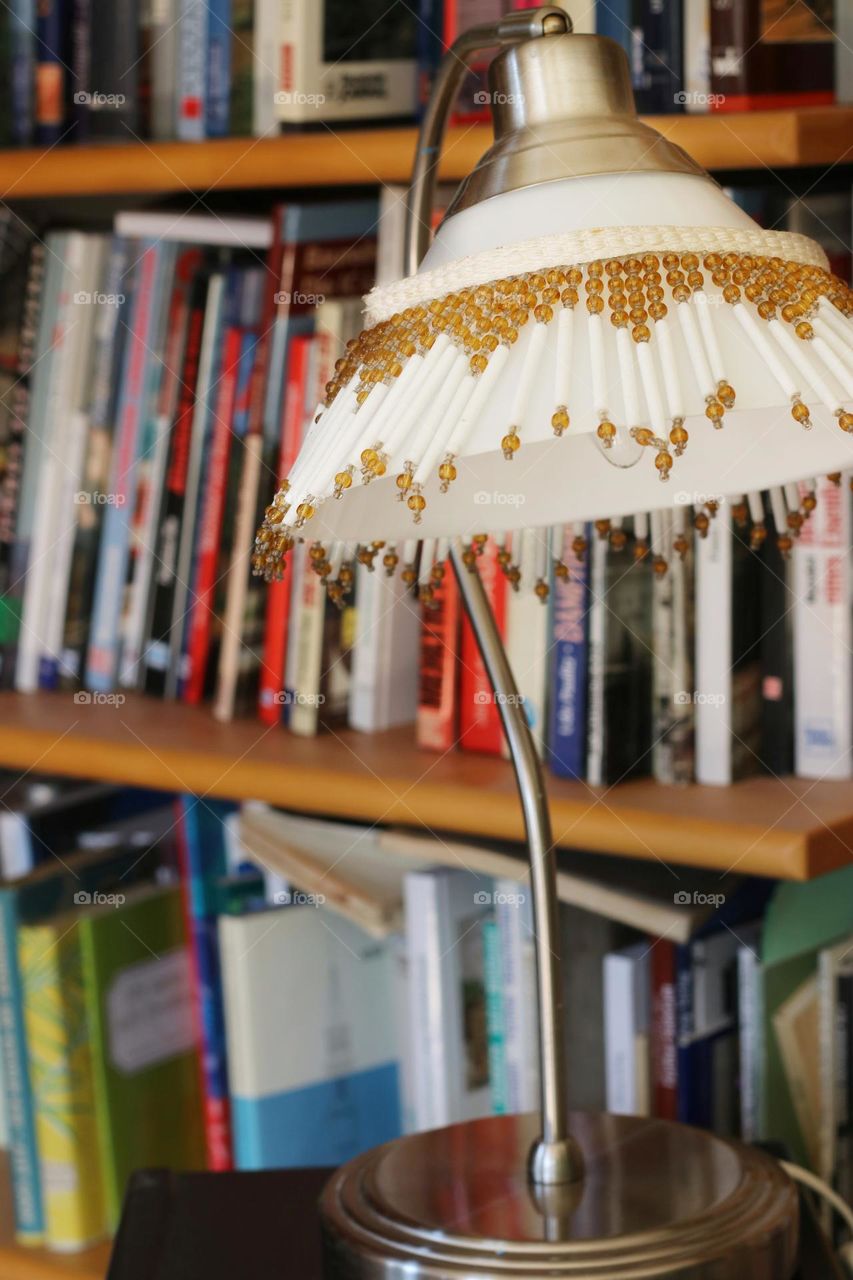 Reading lamp with pearls on a white lampshade in front of a bookshelf