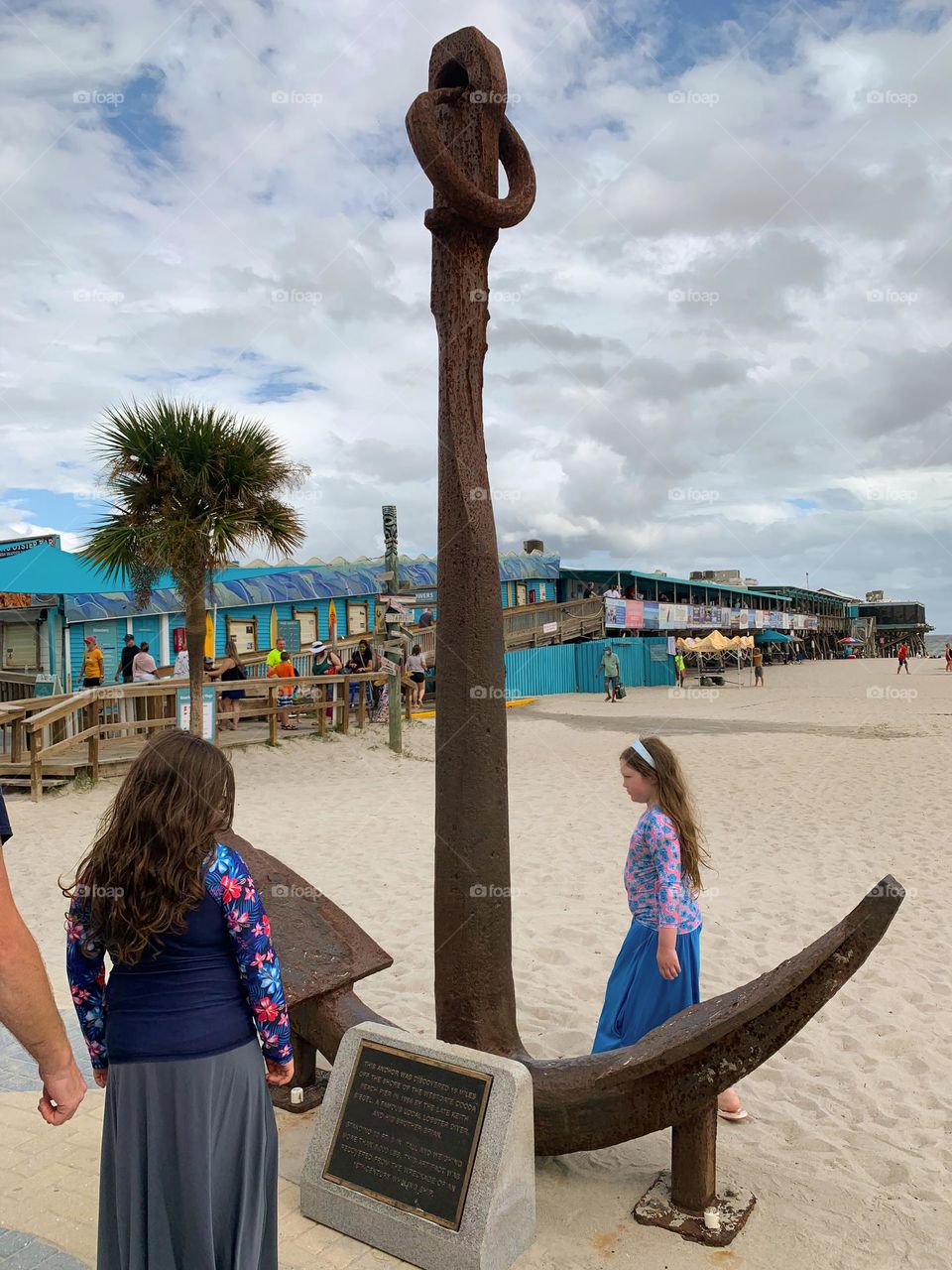 Visiting the visitor touristic pier in Cocoa Beach as a family for the first time in central eastern Florida looking at the immense old historic tall anchor with many shops, restaurants, business and boutiques at the Atlantic Ocean beach with crowd.