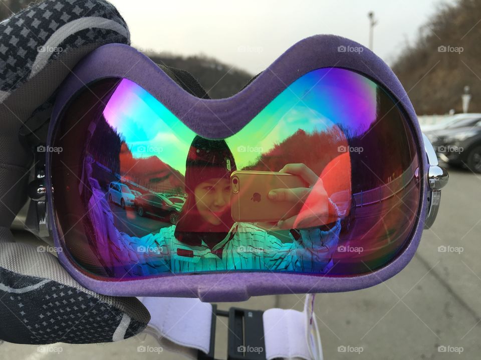 Reflection of woman holding mobile phone in ski goggles