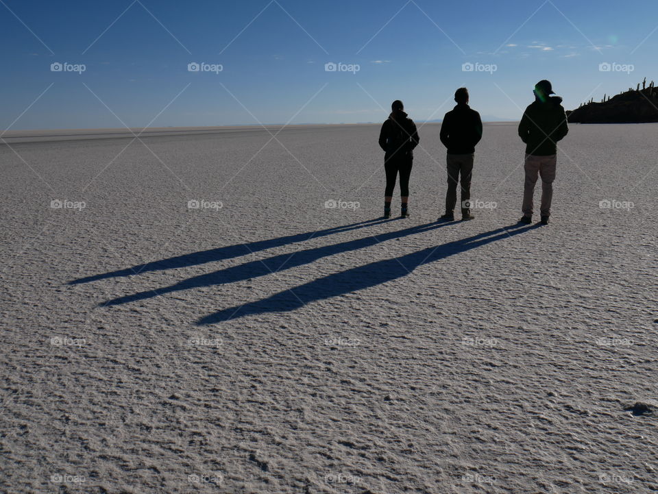 Three tourists and their shadows in the salt flat in Salar de Uyuni in Bolivia