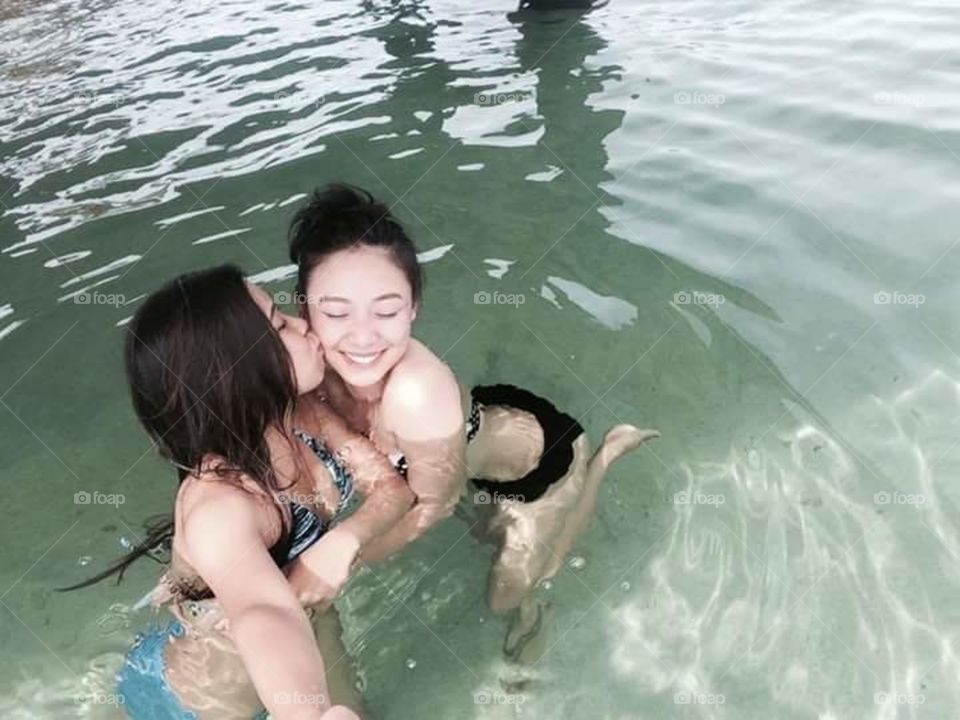 Two female friend kissing in water and taking selfie
