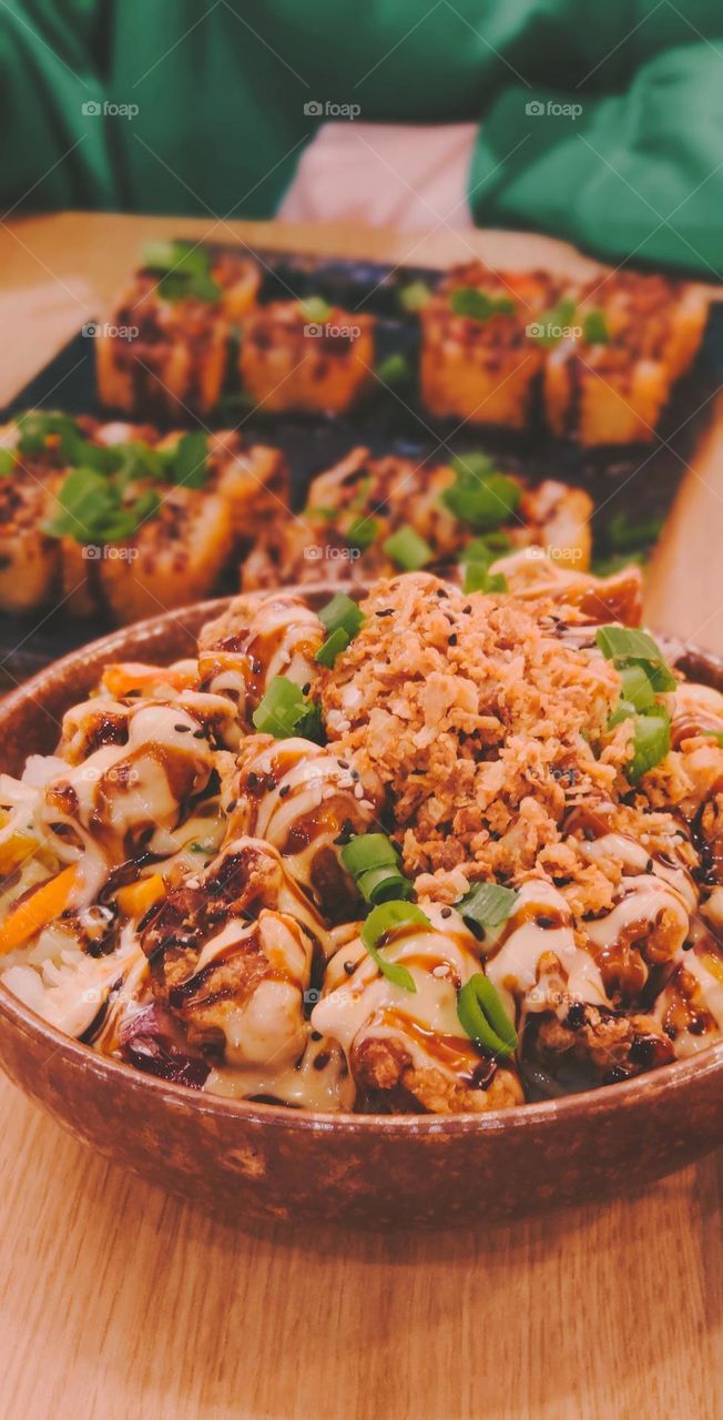 One plate of traditional Asian rice with chicken, soy sauce and green onions on a table in a restaurant with sushi and an unrecognizable girl sitting on a blurred background, close-up side view. Asian food concept.