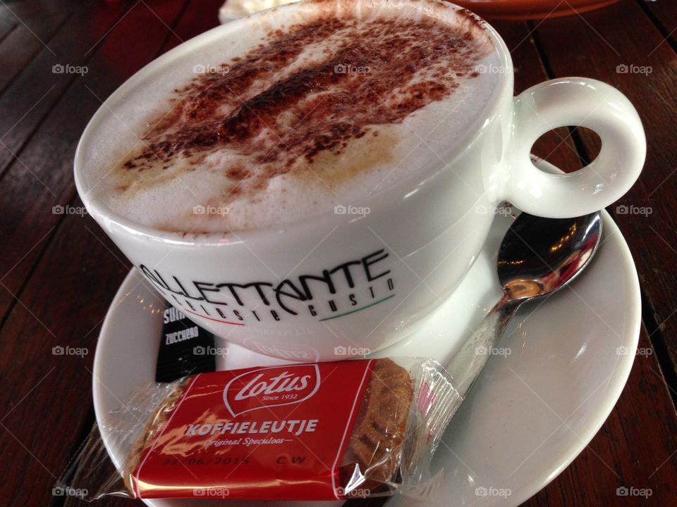 A cup of cappuccino with a cookie on the side