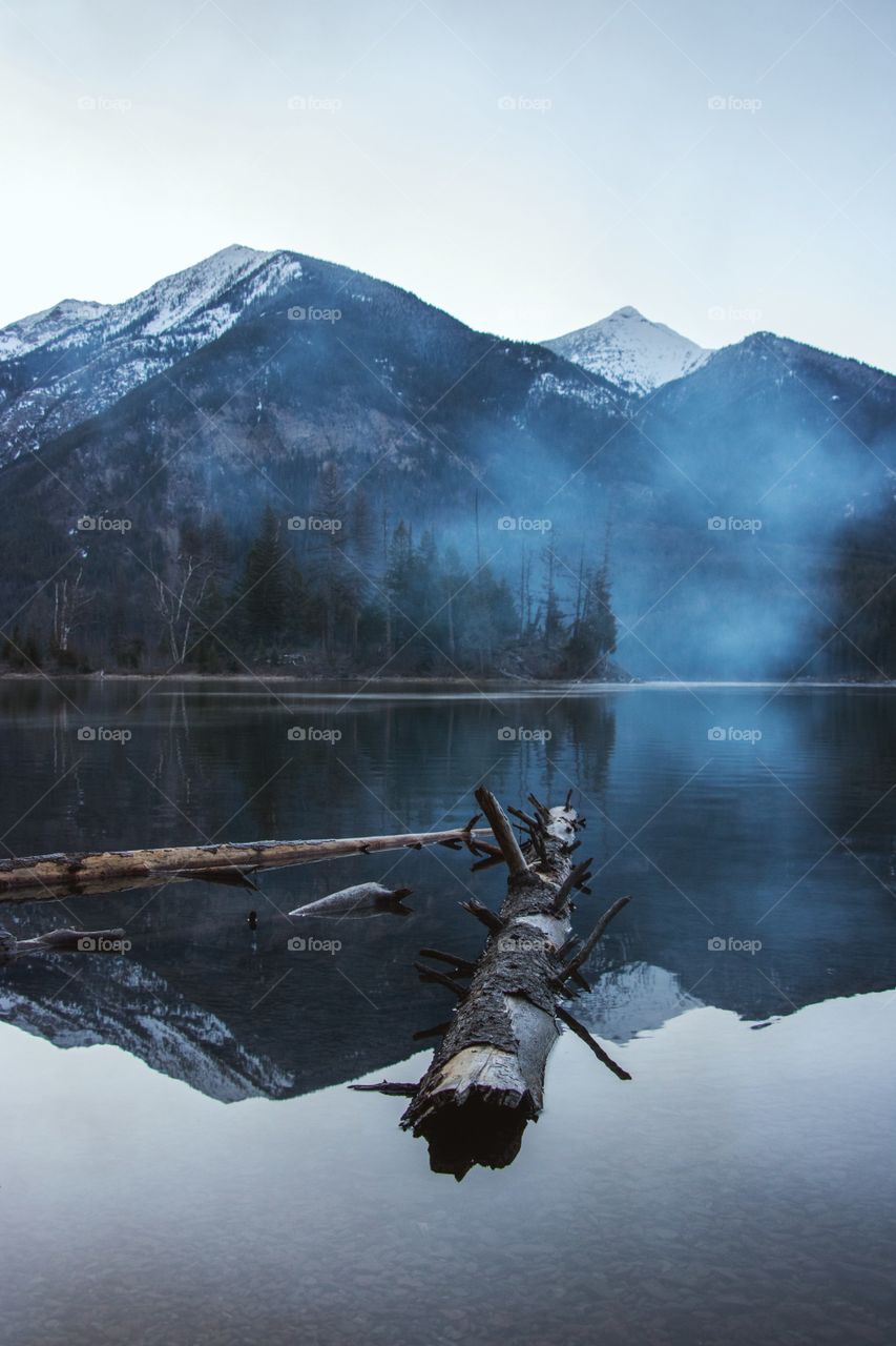 The reflection of snowy mountains on a foggy lake at dawn. 