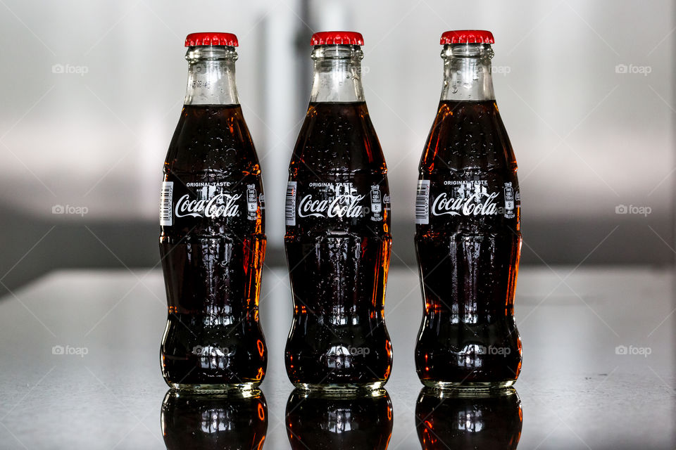 Three cold glass bottles of cold Coca-Cola on a shiny countertop 