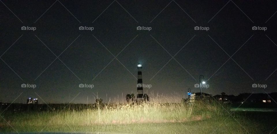A lighthouse standing in a field at night time.