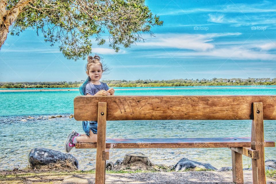 Little girl on wooden bench near sea