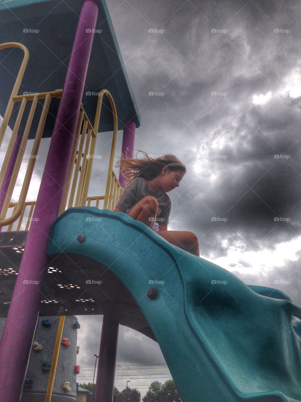 Slide into the storm . Girl sliding down a slide and storm clouds in the background. 