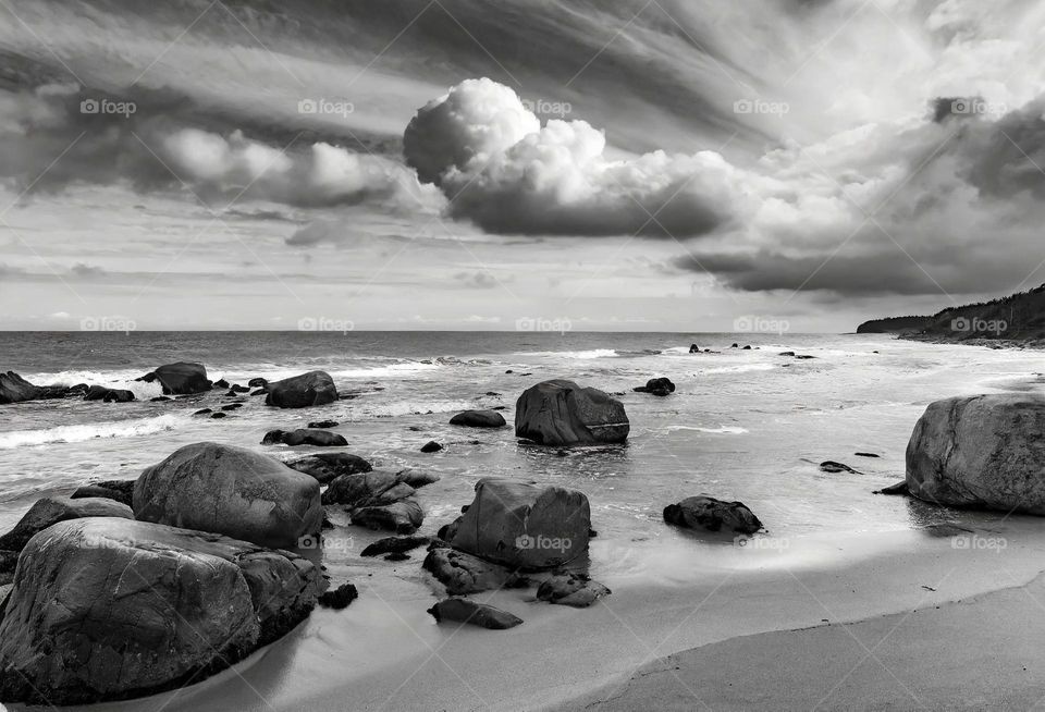 A black and white photograph of a beach with rocks and boulders 