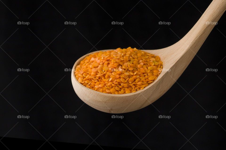 Wooden spoon filled with lentils on black background