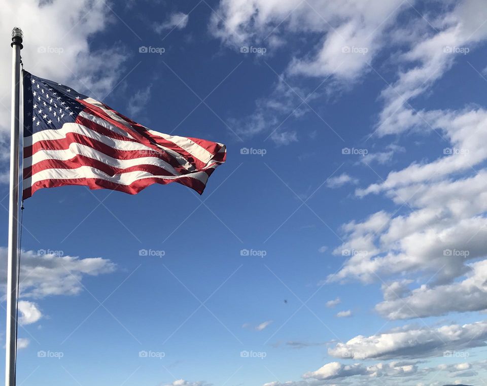 American Flag flying high into a blue, cloudy sky