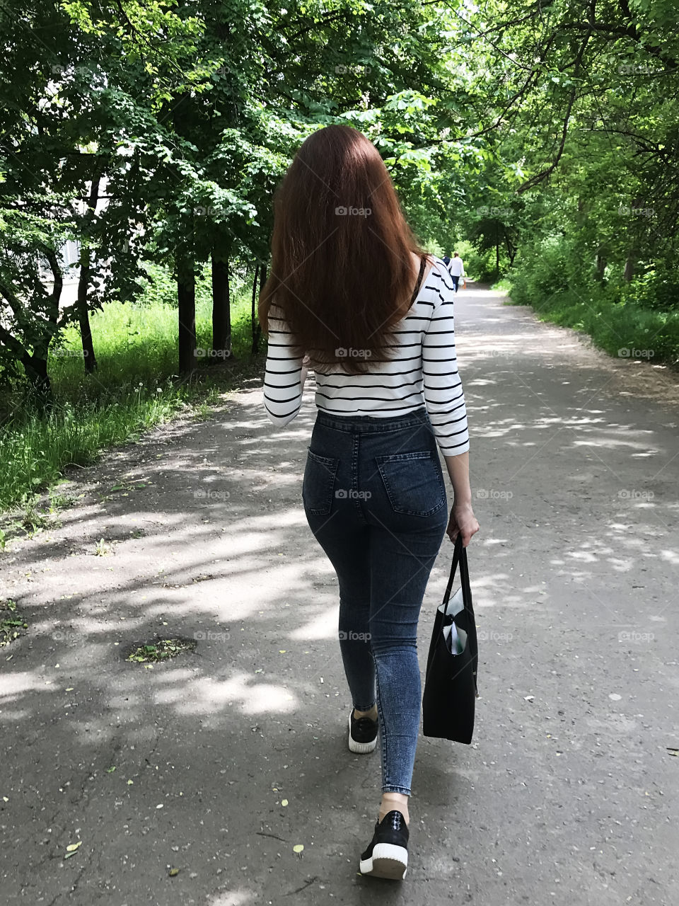 Young woman with red hair walking in city park 