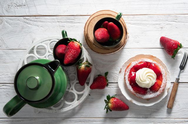 still life colorful food, sweet strawberry cake decorated with cream on a plate, green porcelain service with a cup of tea, homemade cakes