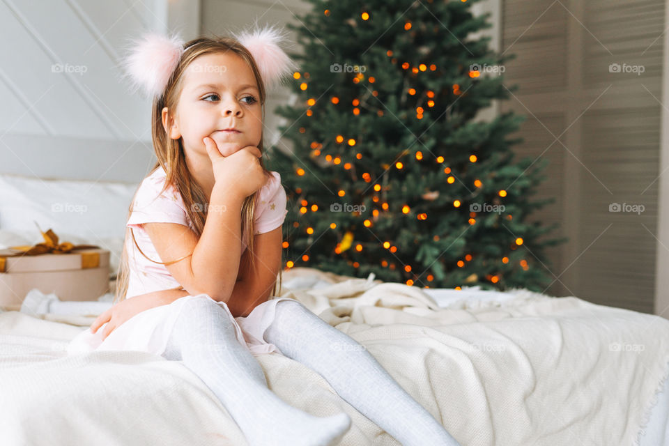 Cute little girl on bed in bedroom with Christmas tree at home 