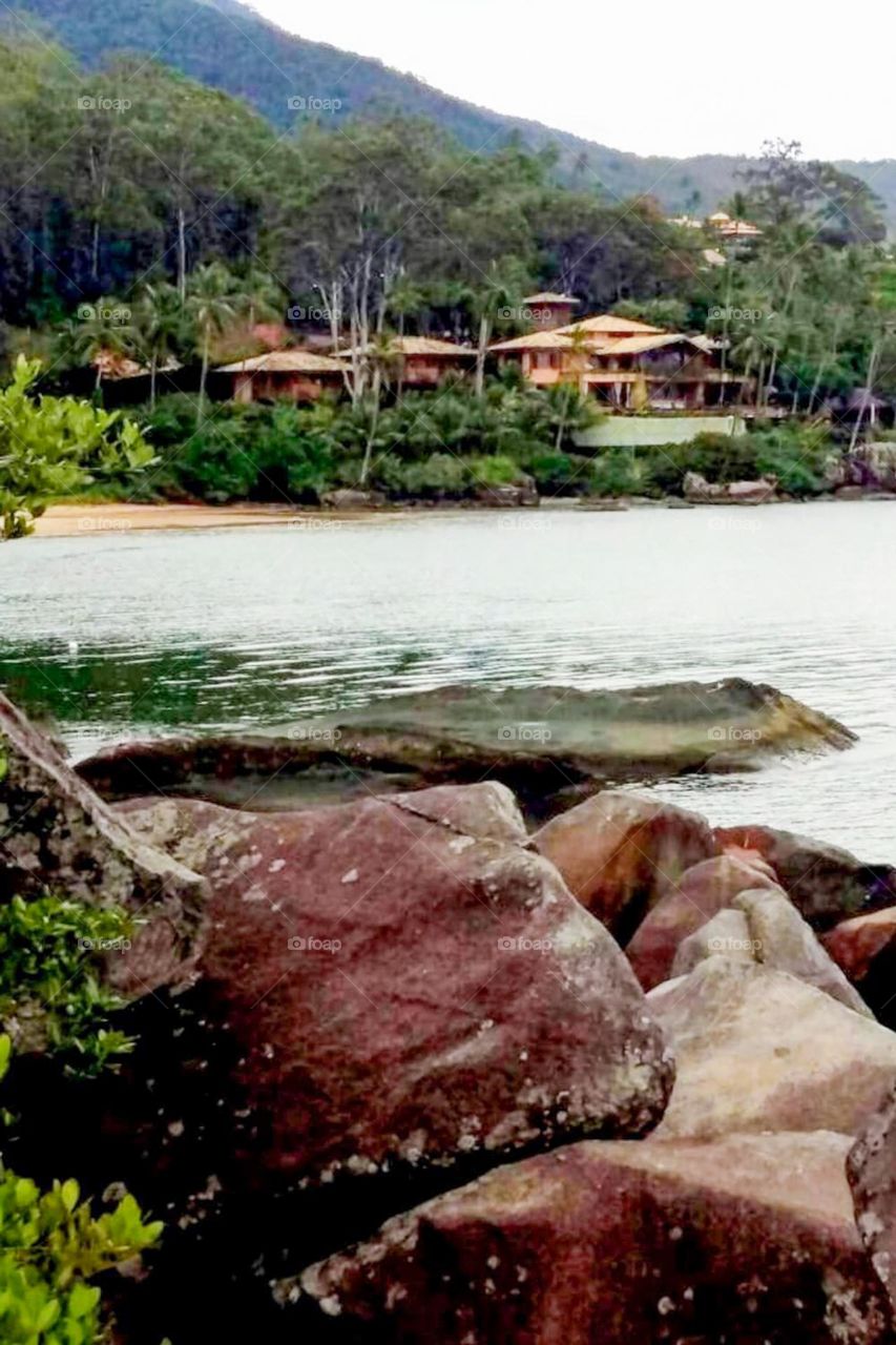 Beach in the Ilhabela Archipelago. In the background summer houses and exuberant vegetation of the Atlantic Forest.