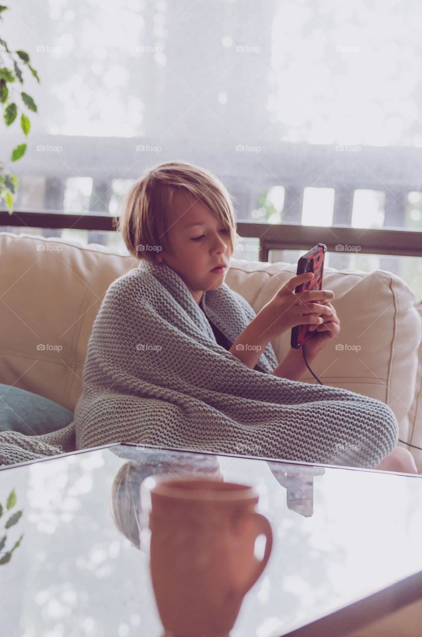 Young boy wrapped in blanket on cell phone 