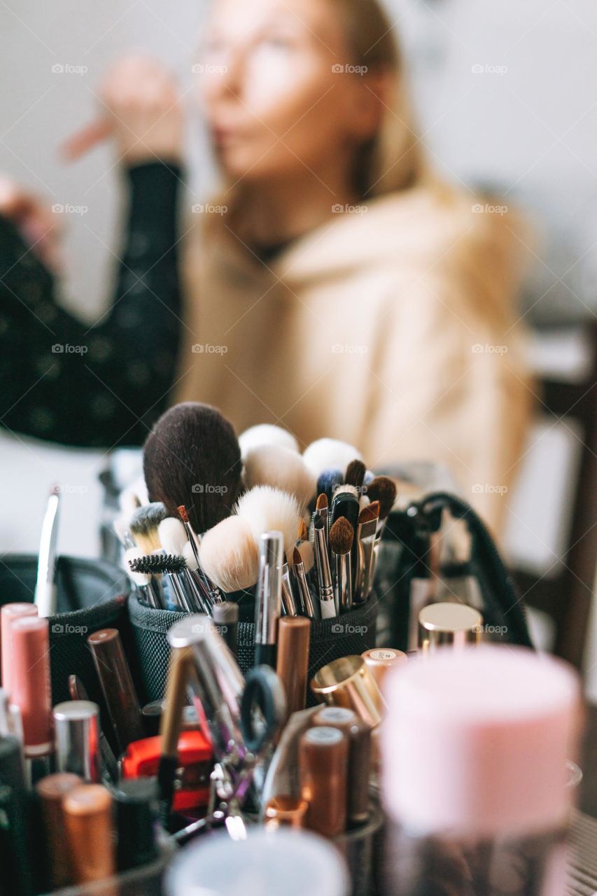 Makeup artist making makeup for woman on background of cosmetic products 