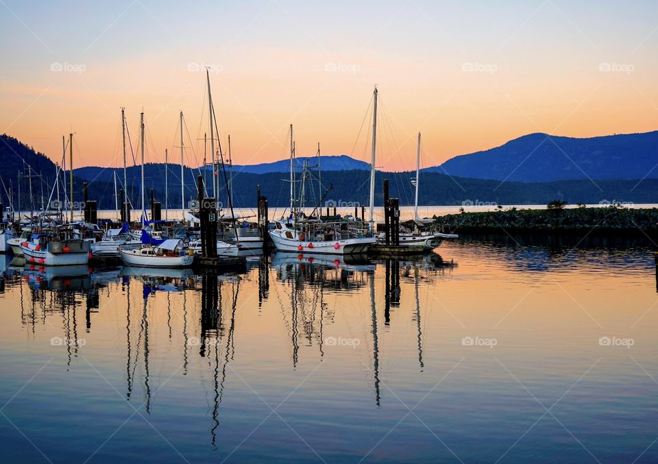 Sailboats reflect on still ocean waters in sunset 