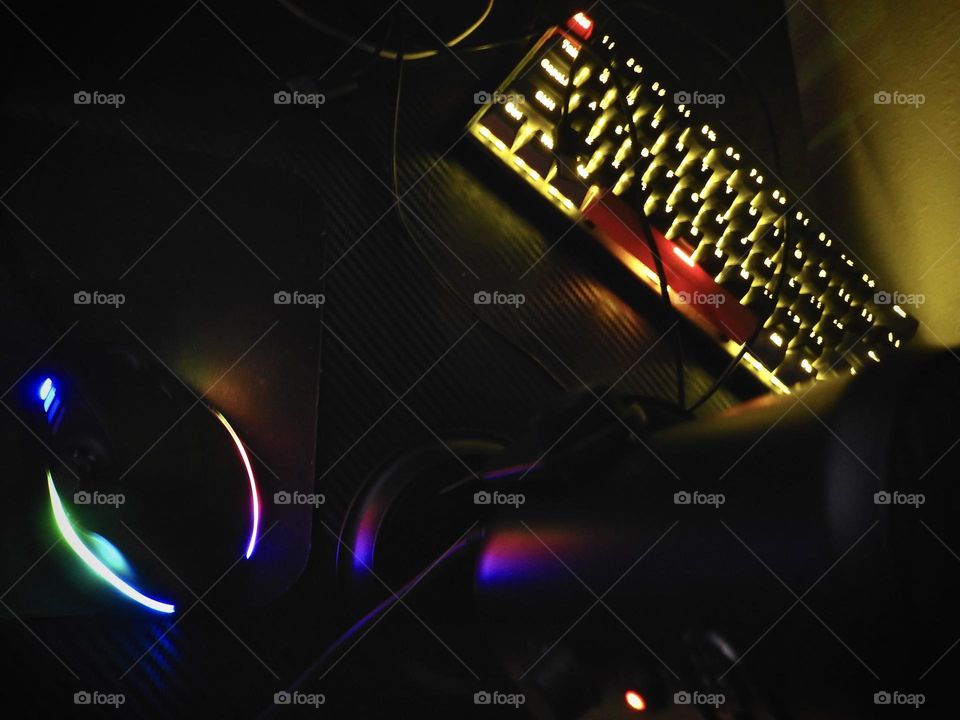 Gaming set showing accessories in a dark room enhancing the beautiful effect with the illuminating of different color lighting through them on a gaming desk.