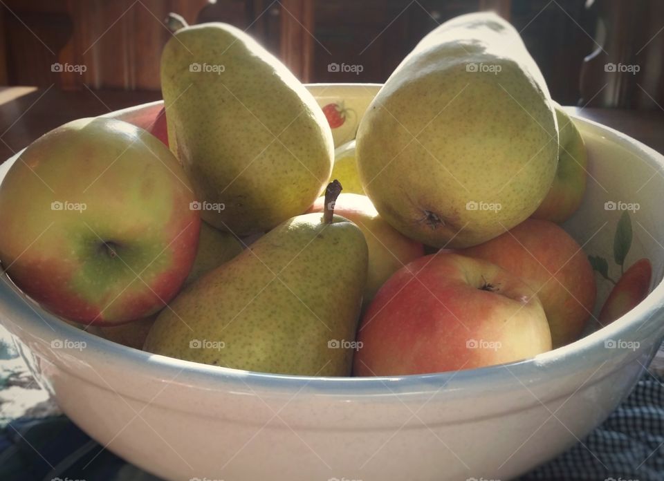 Pears and apples in a big bowl in the middle of the kitchen table in the early morning light