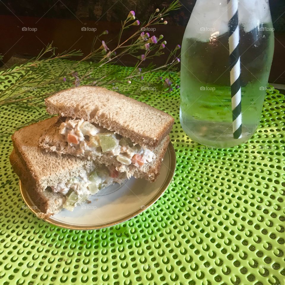 A tasty tunafish salad sandwich on white bread with celery, red bell peppers, and pickles with ice water on a lime green placemat. USA, America 