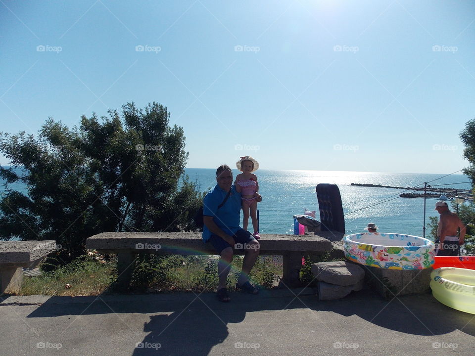 Father and daughter sitting on bench at seaside