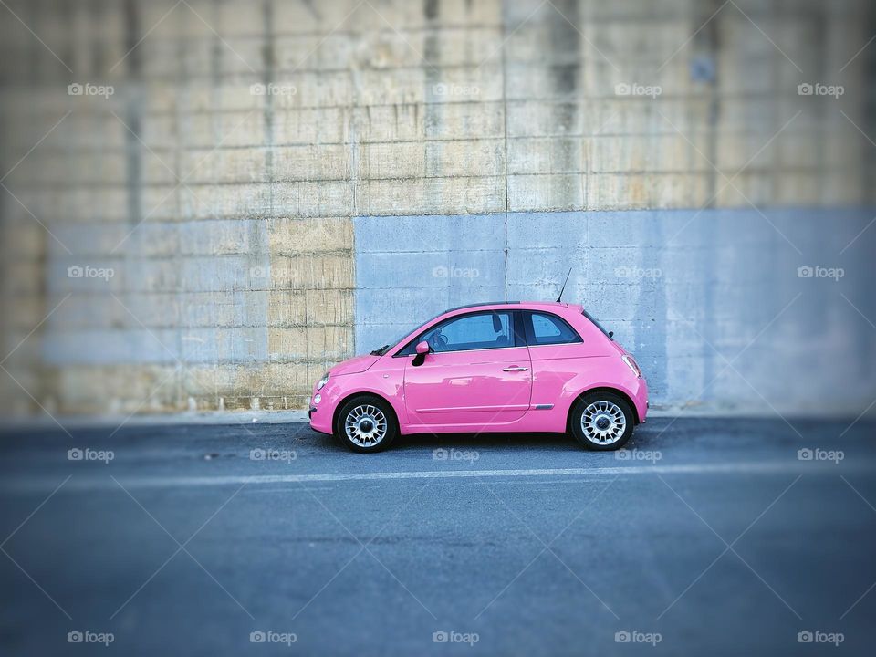 adorable pink FIAT 500 parked in front of a gray wall