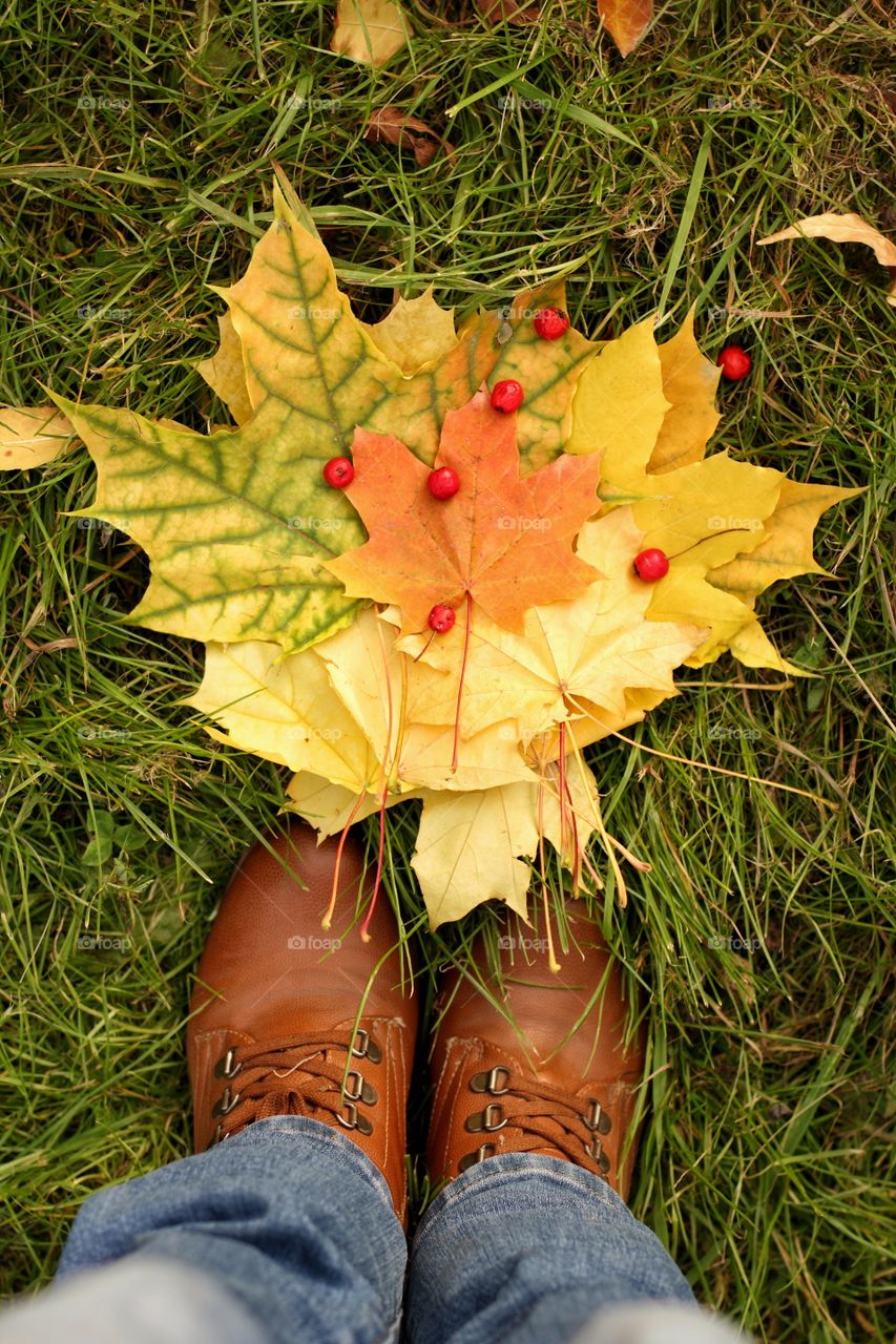 Selfie in brown boots on the lawn with red and yellow maple leaves and hawthorn berries in the fall
