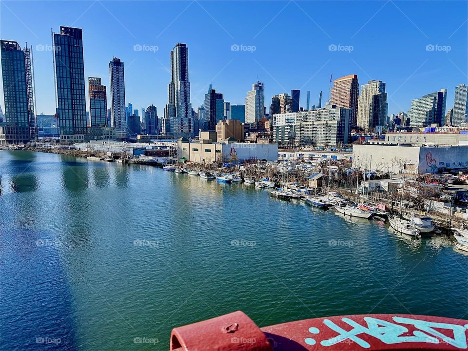 This is picturesque „Newtown Creek“ with a great variety of boats that are tied to the shore here seen from the „Pulaski Bridge“ that connects „Greenpoint“, Brooklyn to LIC, Queens. In the distance you can see „Manhattan“. 2024. Hypnotic Productions