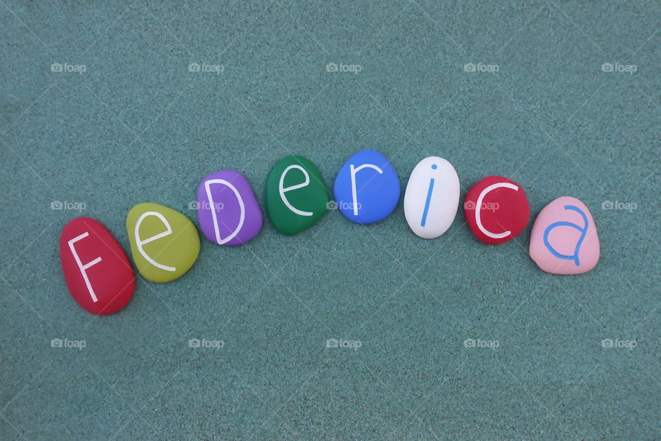 Federica, italian feminine given name with colored stones over green sand
