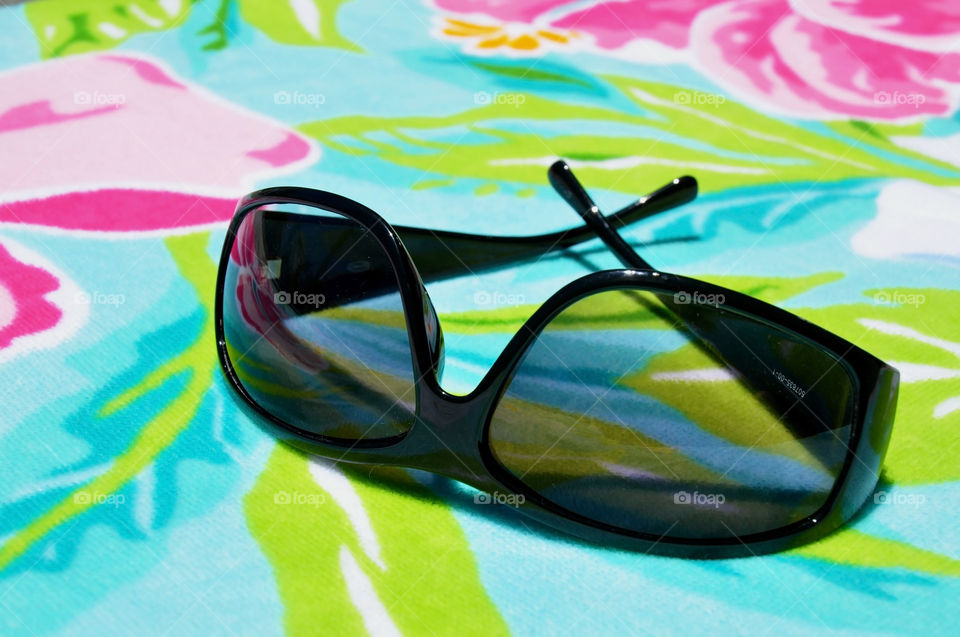 A pair of sunglasses on a colorful beach towel. Summertime concept.