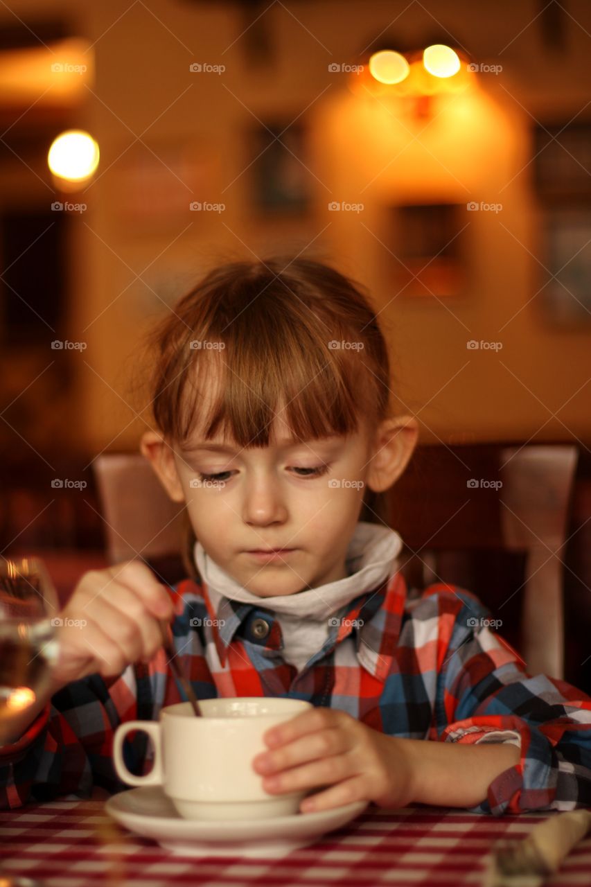 Little girl at the table stirs sugar in a white cup of tea