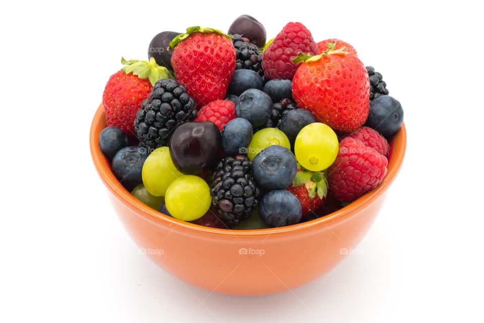 Ceramic bowl full of mixed forest fruits (blueberries, raspberries, blackberries and strawberries), cherries and grapes. White background