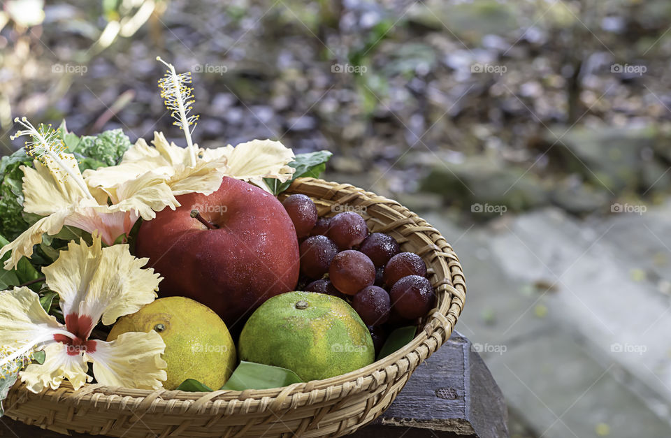 Apple, Orange and grape in weave bamboo baskets with floral decorations Background blurry trees.