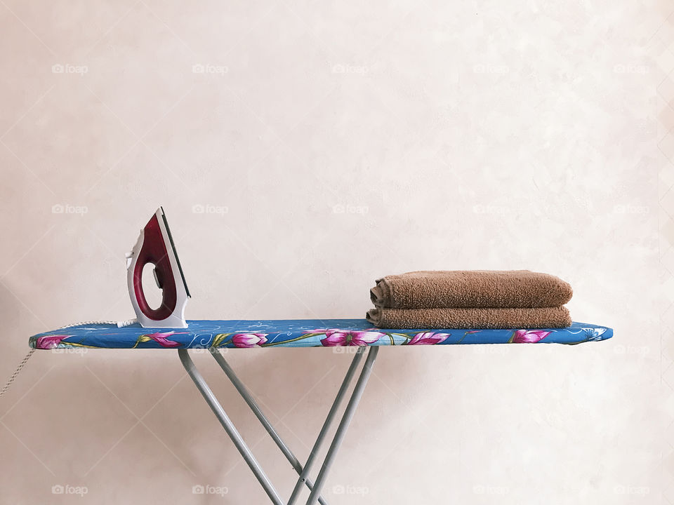 Ironing, minimal concept, iron and laundry on ironing board on pastel wall background 
