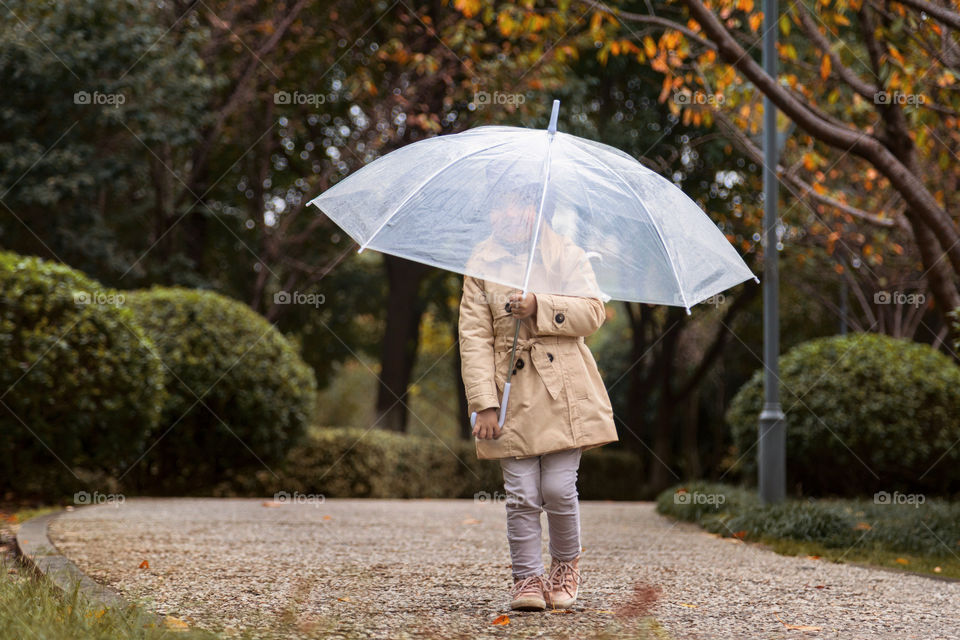 Stylish little girl walking in the park with umbrella 