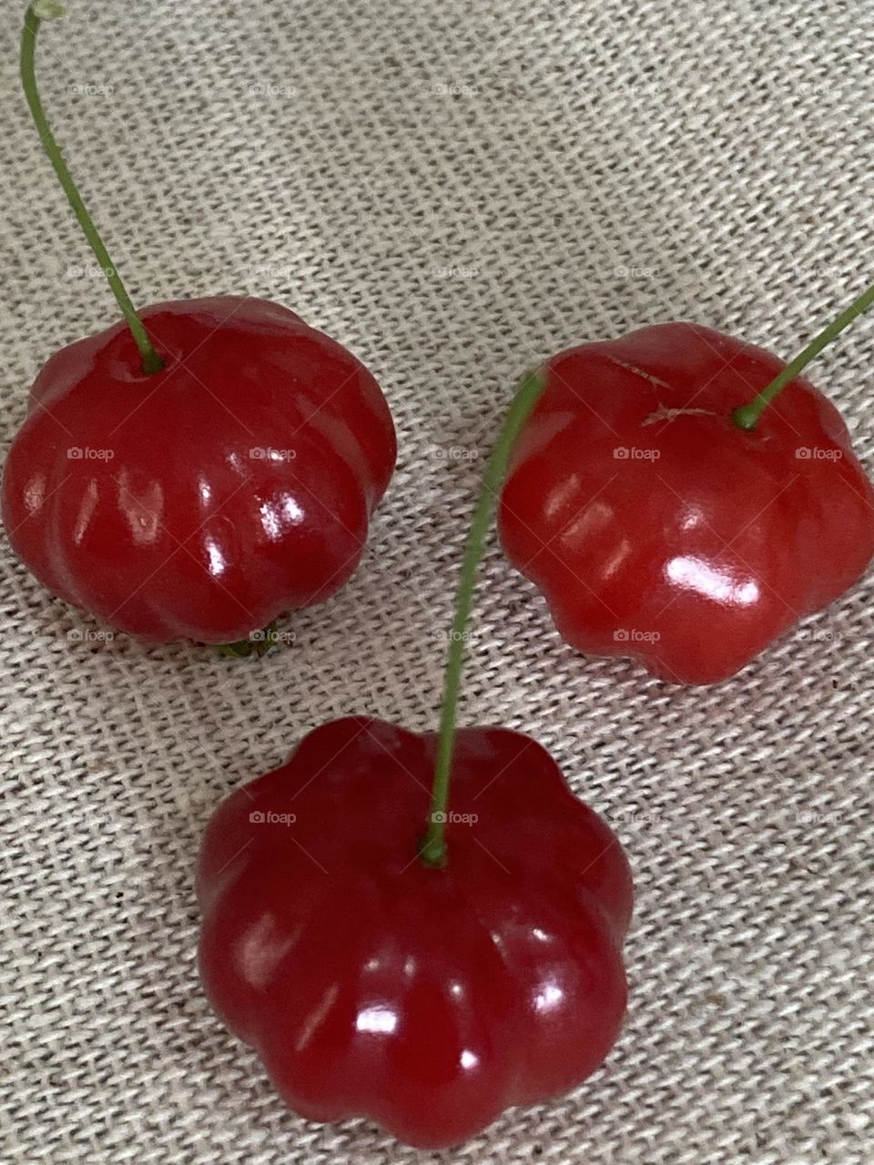 Trio de frutas vermelhas de pitanga sobre uma mesa coberta com toalha de bege de algodão.