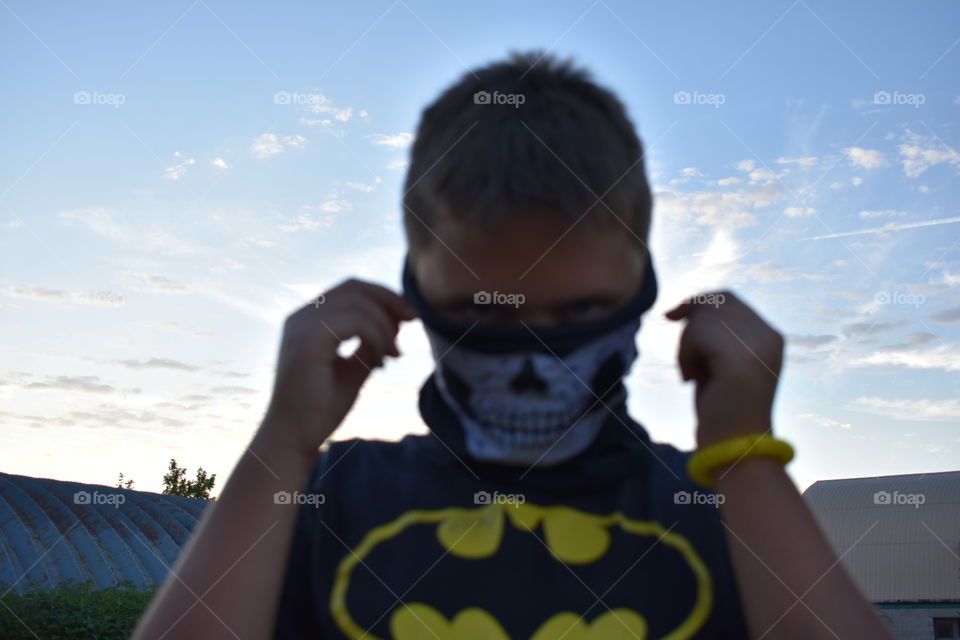 Boy putting on a skull bandana against blue sky 