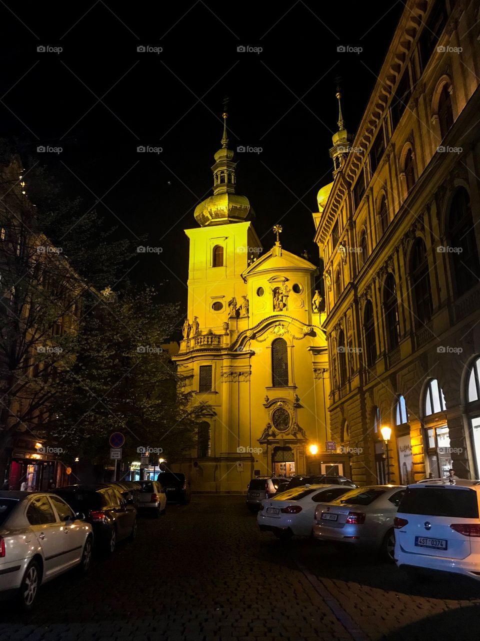 A church on the street at night,cars parked, buildings at 2 side,a few yellow street lights, in the very dark sky. I saw it when I walking around  the streets in the city 